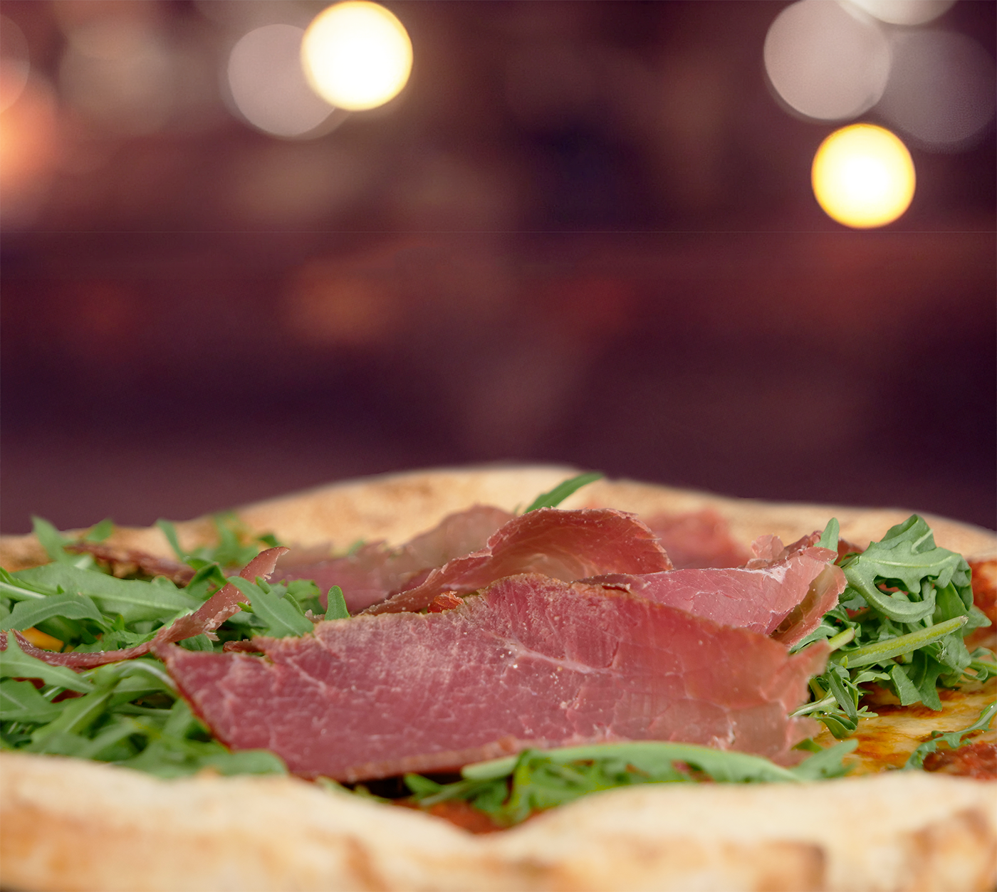 Pizza del Valais seitlich fotografiert – feines Bündnerfleisch auf frischem Rucola, serviert auf fluffigem Boden.