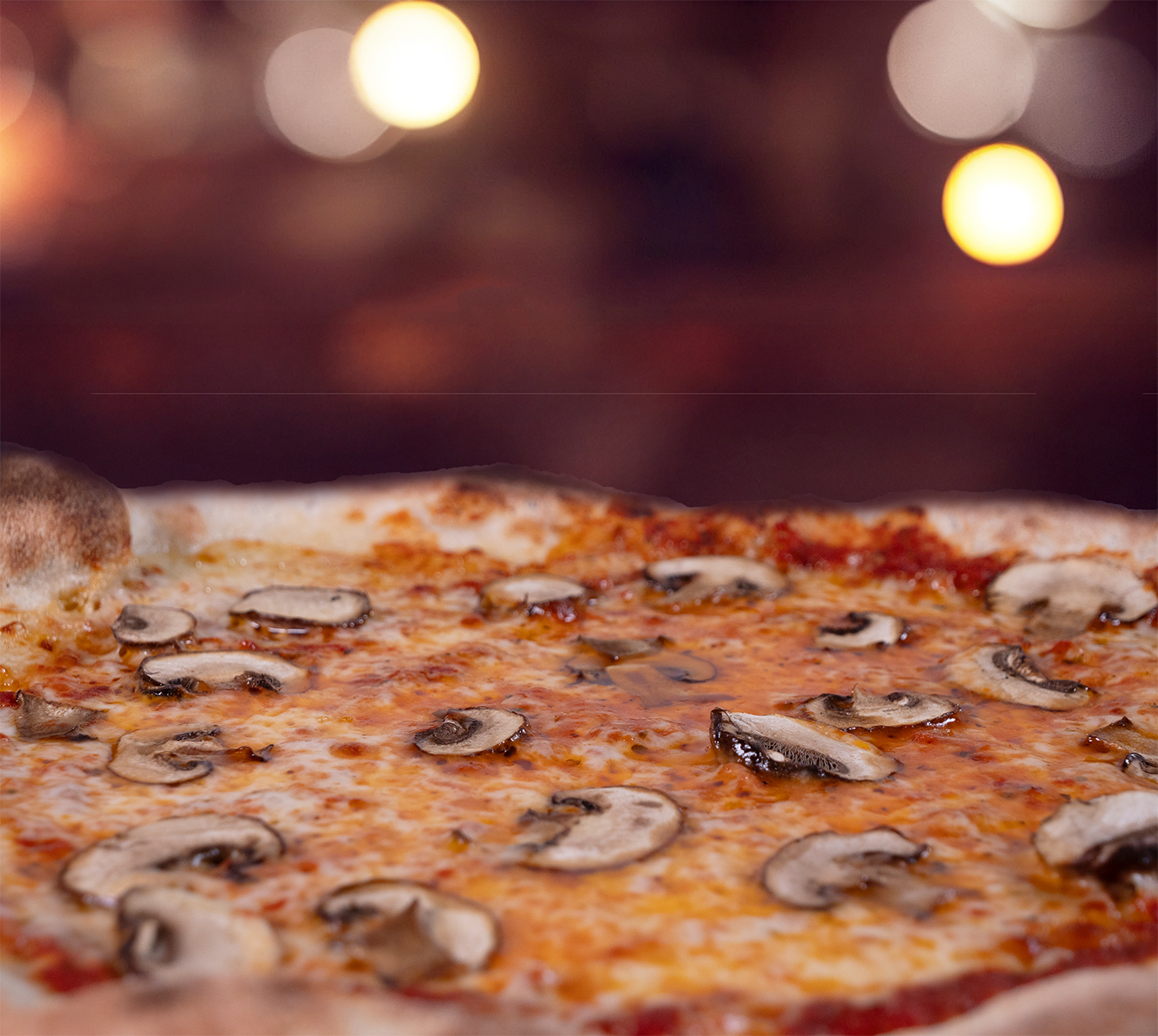 Pizza Funghi seitlich fotografiert – fluffiger Rand, geschmolzener Käse mit frischen Pilzen, warme Lichtstimmung im Hintergrund.
