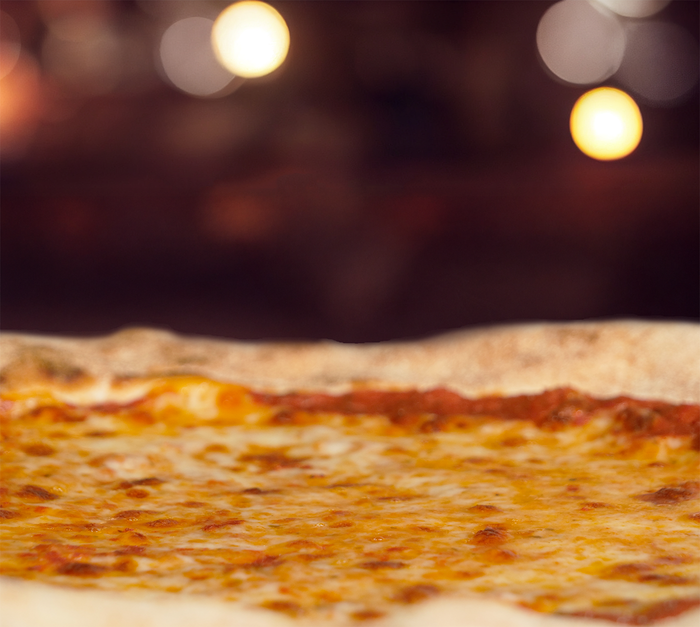 Pizza Margherita seitlich fotografiert – dampfend heiss, mit goldbraunem Rand und geschmolzenem Käse.