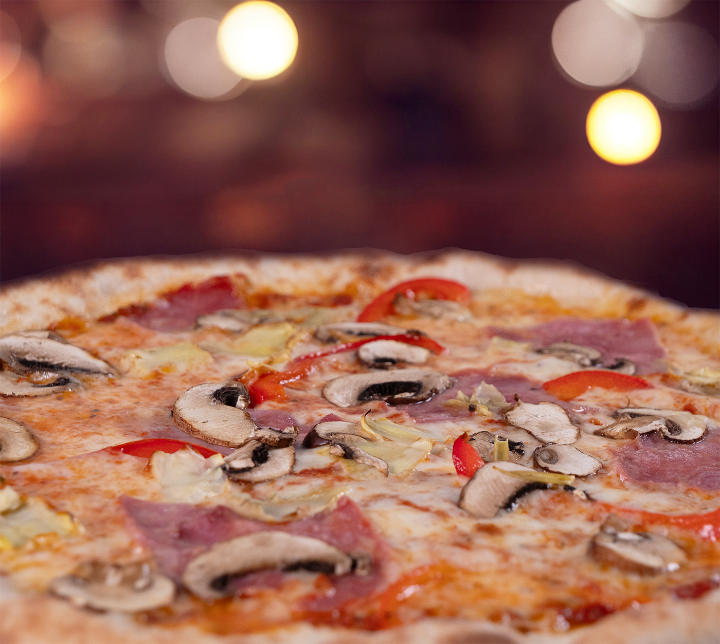 Pizza Quattro Stagioni seitlich fotografiert – fluffiger Rand, bunte Kombination aus Schinken, Pilzen, Peperoni und Artischocken, leicht geschmolzener Käse, stimmungsvolle Beleuchtung.