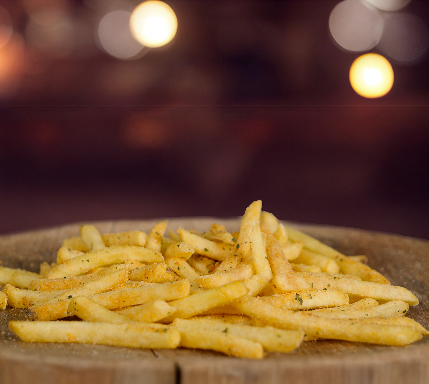 Nahaufnahme gewürzter Pommes auf Holzbrett – leicht schräg fotografiert, im Hintergrund verschwommenes Lichtambiente.