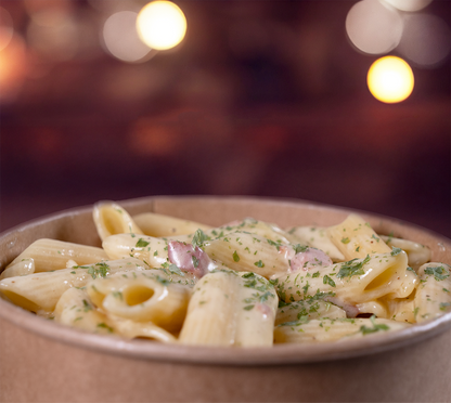 Penne Carbonara seitlich fotografiert – dampfend, cremig und mit Kräutern bestreut, perfekt angerichtet im Take-Away-Stil.