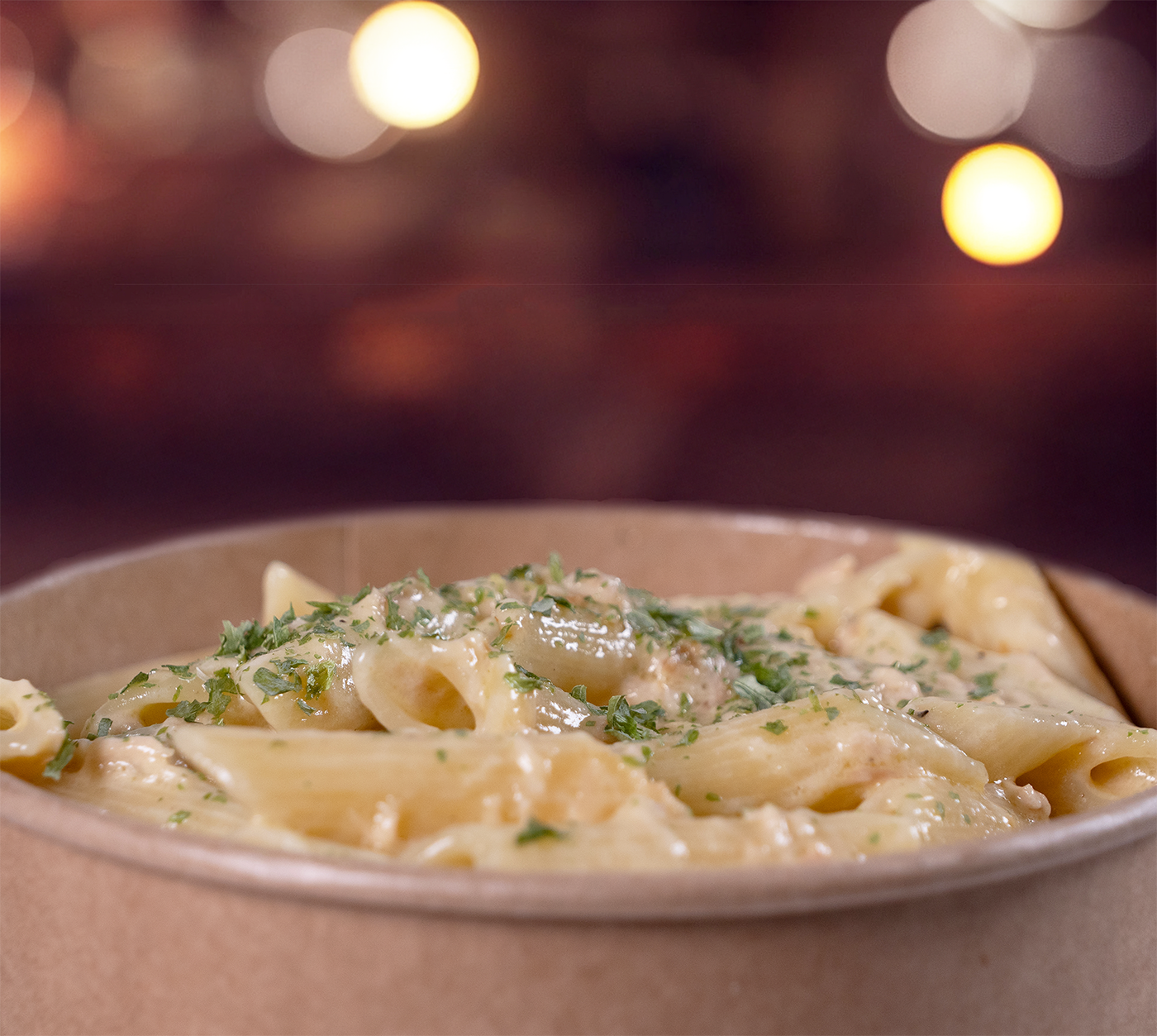 Penne mit Rahmsauce seitlich fotografiert – dampfende Pasta mit Pilzen in cremiger Sauce, serviert im rustikalen Take-Away-Becher.