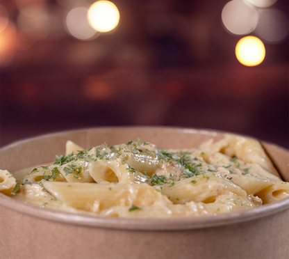 Penne mit Rahmsauce seitlich fotografiert – dampfende Pasta mit Pilzen in cremiger Sauce, serviert im rustikalen Take-Away-Becher.