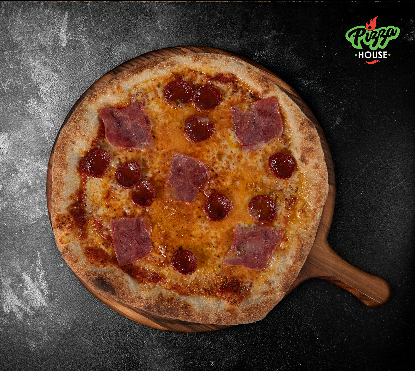 Pizza Lina von oben – mit scharfer Salami, Schinken und goldbraunem Käse belegt, serviert auf Holzbrett vor dunklem Untergrund.