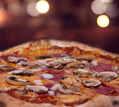 Pizza Prosciutto e Funghi seitlich fotografiert – geschmolzener Käse, zarte Schinkenstücke und frische Pilze auf fluffigem Teig, stimmungsvolle Beleuchtung im Hintergrund.