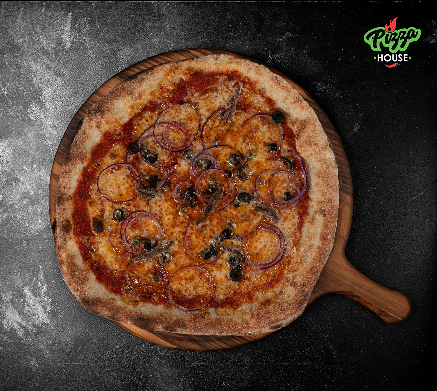 Pizza Siciliana von oben – belegt mit Sardellen, schwarzen Oliven, roten Zwiebelringen und Kapern auf goldbraunem Käse, serviert auf Holzbrett vor dunklem Hintergrund.