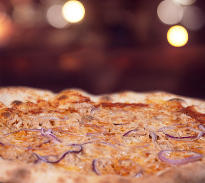 Pizza Tonno seitlich fotografiert – knuspriger Rand, saftiger Belag mit Thunfisch und roten Zwiebeln, serviert auf Holzbrett, warme Atmosphäre.