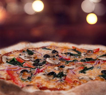 Pizza Verdura seitlich fotografiert – luftiger Rand, buntes Gemüse in Kombination mit geschmolzenem Käse, mediterrane Farben, stimmungsvolle Hintergrundbeleuchtung.